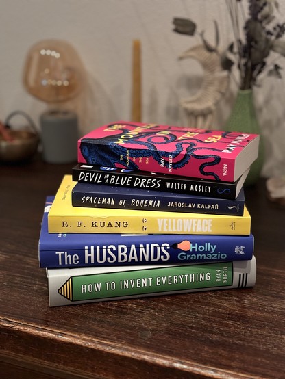 Neatly stacked pile of six book. From the top to the bottom:

- The Mountain In The Sea by Ray Nayler
- Devil In A Blue Dress by Walter Mosley
- Spaceman Of Bohemia by Jaroslav Kalfař
- Yellowface by R.F. Kuang
- The Husbands by Holly Gramazio
- How To Invent Everything by Ryan North