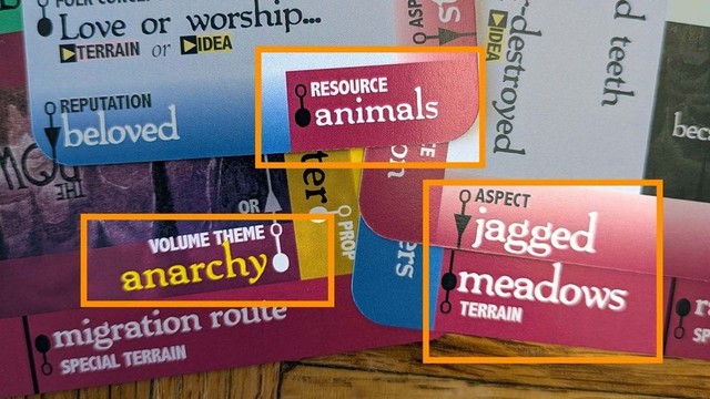 A set of Downcrawl Deck cards displays the prompts "Volume Theme: Anarchy," "Resource: Animals," and "Aspect: Jagged Meadows."