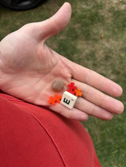 My hand holding one small
rock, three red puzzle pieces and a Scrabble
tile E.