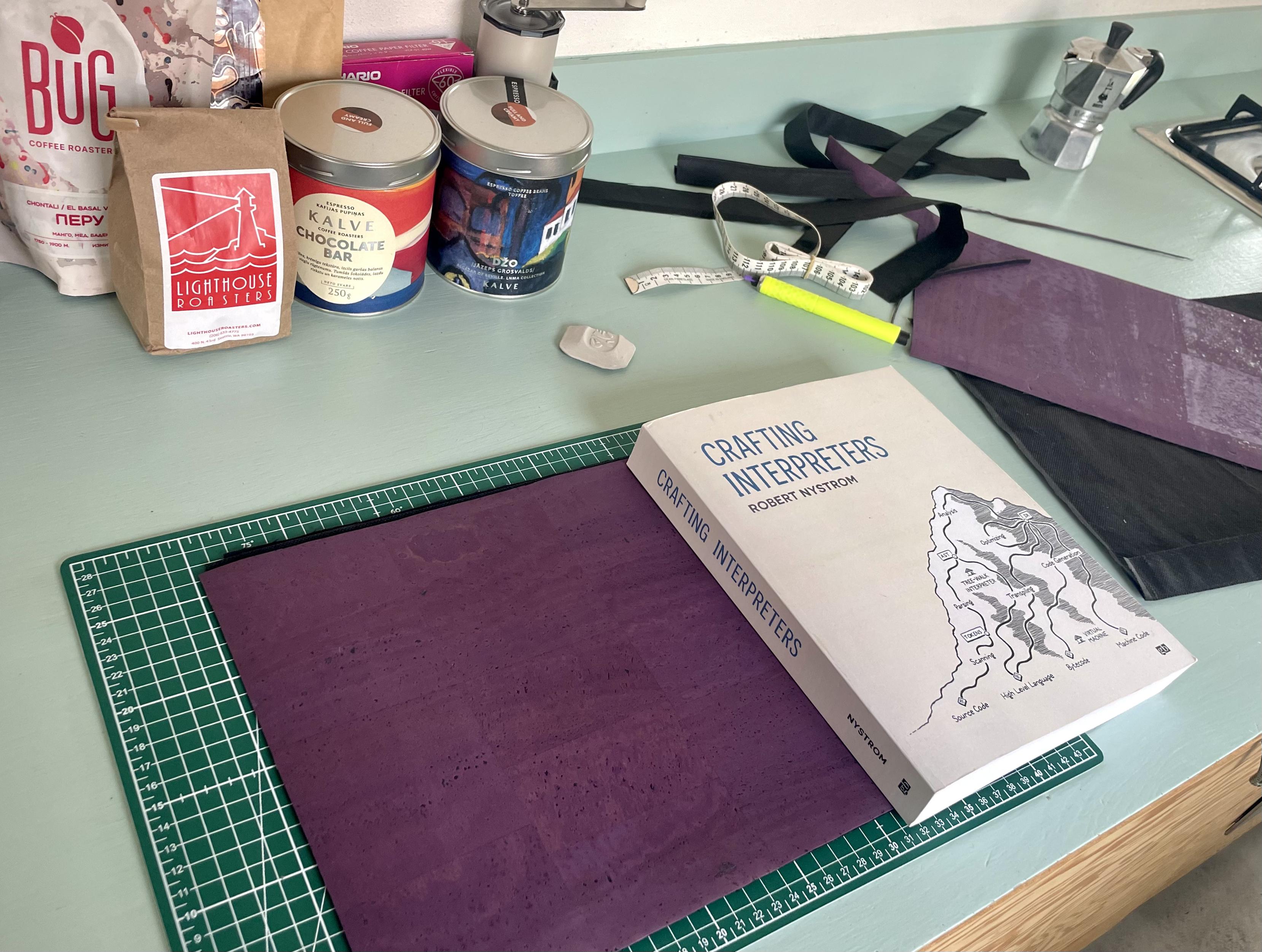 "Crafting Interpreters" book being used as the perfect size weight to press down sewing project layers. (no book has been harmed. too much coffee in the background)