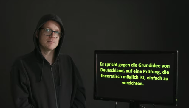 Nico Semsrott vor einem Monitor mit der Aufschrift "Es spricht gegen die Grundidee von Deutschland, auf eine Prüfung, die theoretisch möglich ist, einfach zu verzichten."
