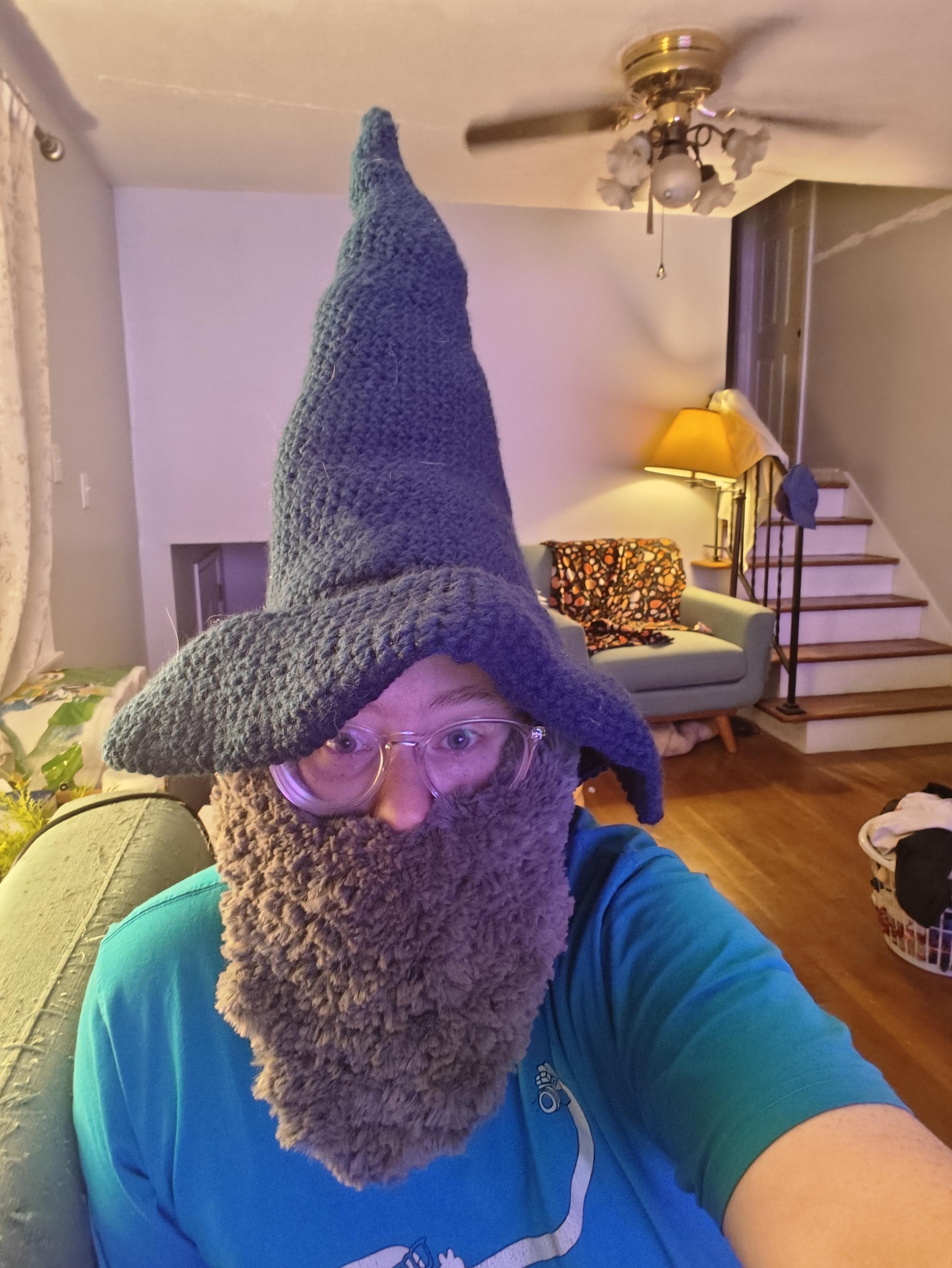 A photo of myself, I have a dark blue crocheted wizard hat and a crocheted beard made with a fuzzy grey yarn.