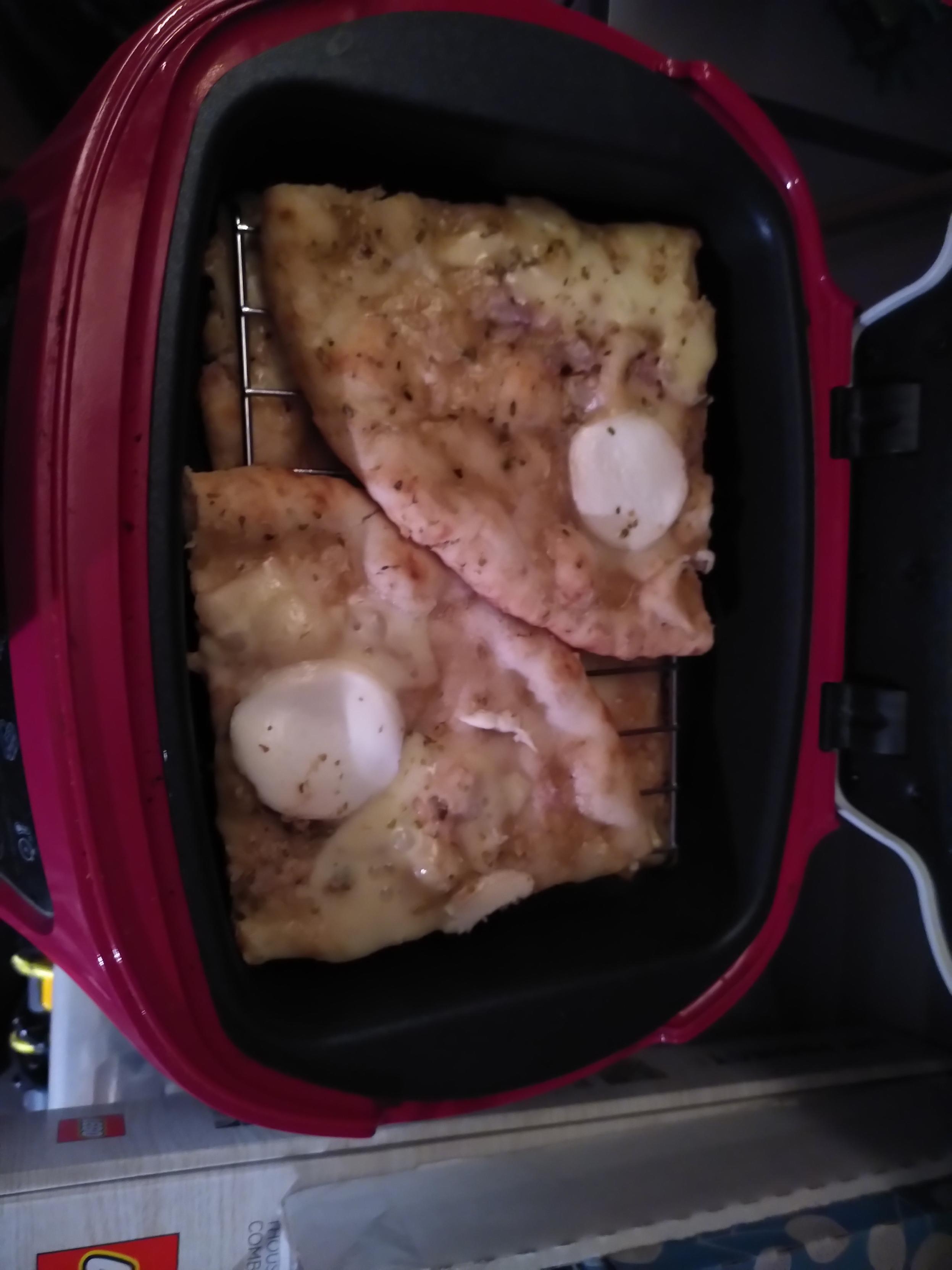 A pizza placed in a small electric oven, ready to be cooked. The oven is tefal's cake factory, inside is just enough space for a brownie cake. The pizza is cut in 4, two slices at the bottom of a baking tin, each with the crust towars the center and two more slice on a grid placed inside the tin, also crust toward the center. The metallic grid is meant to go at the bottom of the oven when used with silicon mold instead of the baking tin so the silicon mold have a surface to stand on