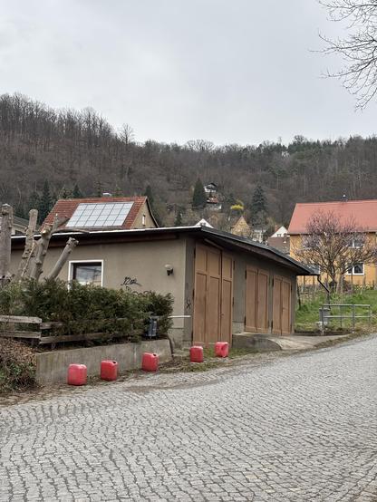 An old shed or garagr with five red canisters neatly put in a row in front of it