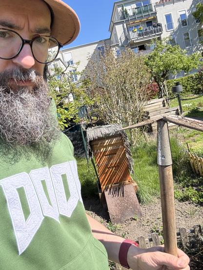 Me standing and holding a garden hoe with a  beehive behind me out in a garden