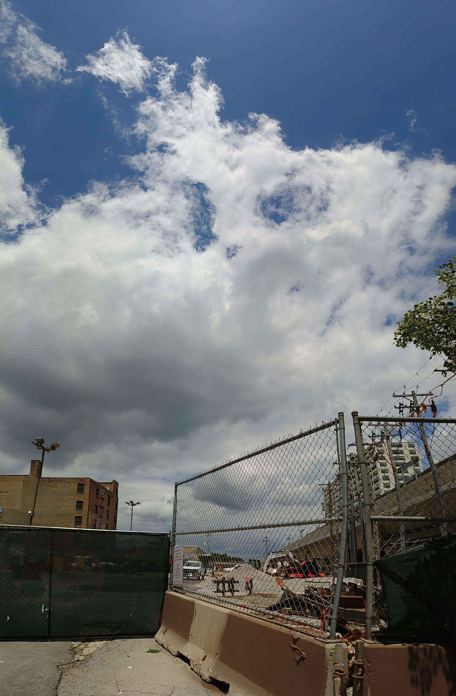 This one is a short vertical panorama taken outside the train station at street level.  There's a fenced off empty lot that's left over from the train station being rebuilt.  More importantly there's a gigantic fluffy bright cloud filling most of the view.  If memory serves I tried to start this photo with the phone pointing more or less straight upward.  It was so bright with the sun overhead I could not really see what I was doing though.