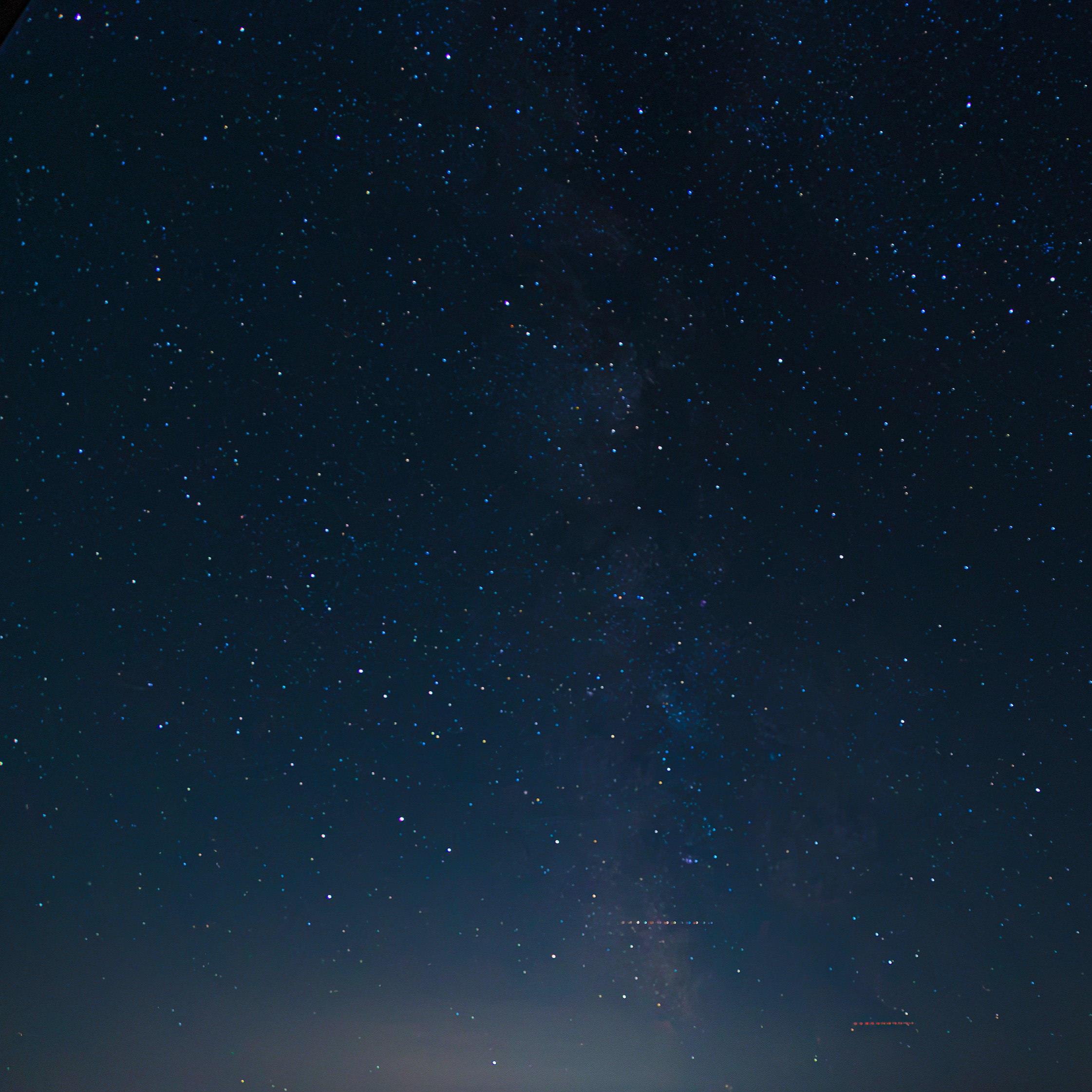 Slightly blurry photo of the milky way with strong light pollution and some planes in the bottom.