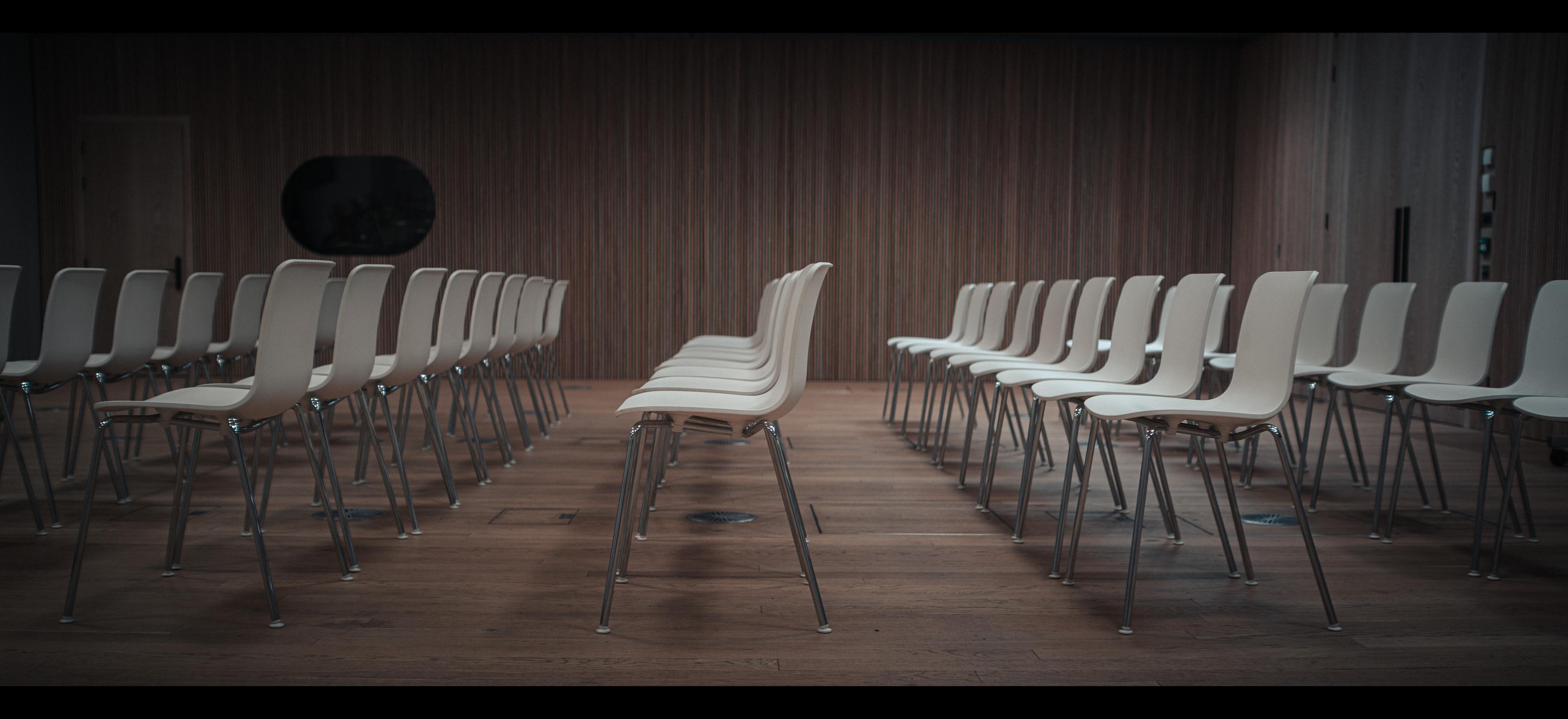 Rows of chairs in a lecture wood grain lined room.