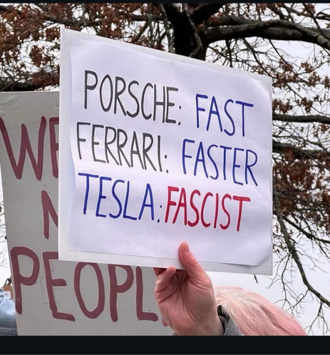 hand held sign reads.
Porsche: Fast
Ferrari: Faster
Tesla: Fascist