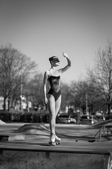 Portrait einer Rollkunstläuferin, die im Skaterpark auf einer Halfpipe steht, in Richtung Sonne schaut und sich mit einer Hand die Sonne von den Augen abhält.
