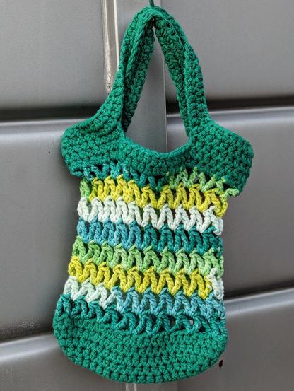 A mini crochet market bag that is green, turquoise, yellow, and white.