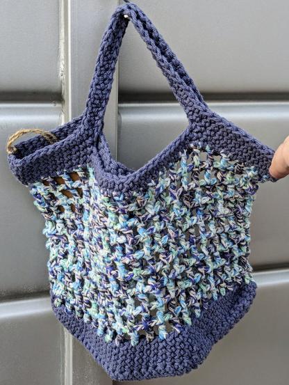 A rectangular crochet market bag in muted shades of blue grey, blue, turquoise, and mint.