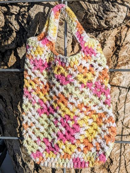A crochet market bag in shades of white, soft green, yellow, orange, and pink.