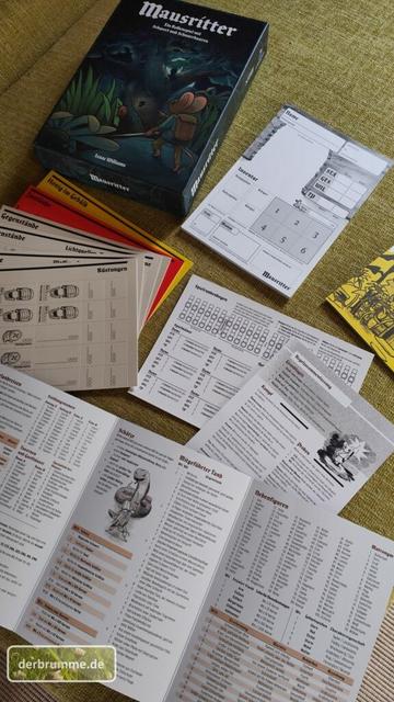 Der Inhalt einer Rollenspielbox liegt ausgebreitet auf einem hellgrünen Stoff. Das System heisst "Mausritter".