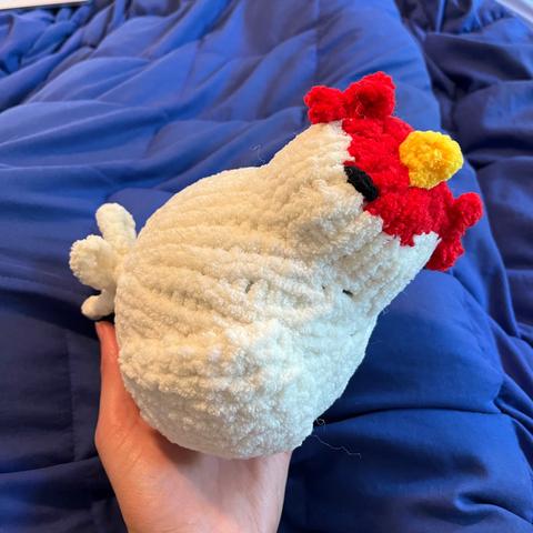 A fuzzy chicken knitted out of chenille yarn, maybe 7 inches wide. She has simple embroidered black eyes and a comb and wattle