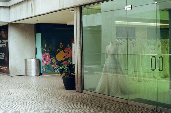 A bridal gown store is closed but lit up after hours in a brutalist architecture shopping pavilion in moderate early evening light.