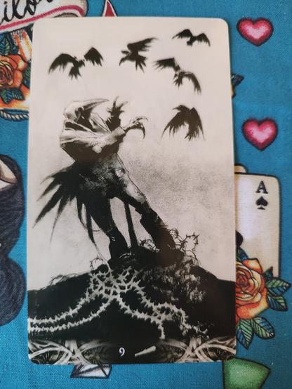 Card from the Murder of Crows Tarot deck. 
Nine of Wands.
A man in a field wearing a crow's mask, trying to keep balance as crows seem to be harassing him.