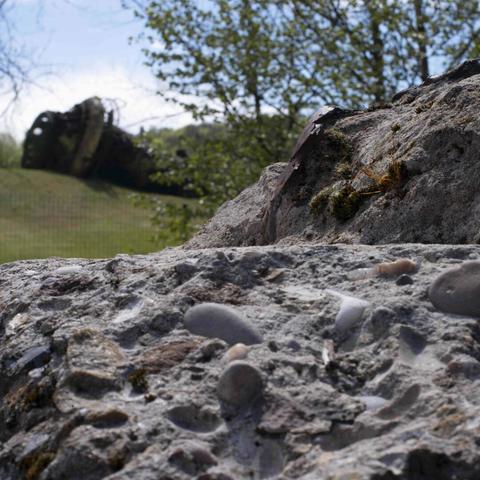 Gros plan sur un bloc de béton, en arrière plan le haut fourneau couché sur le terrain de golf