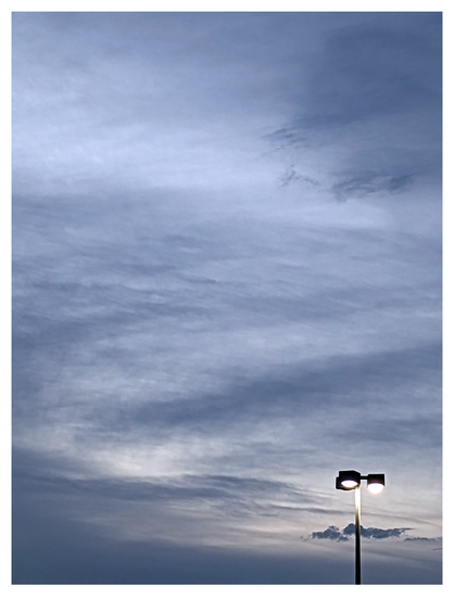 at bottom right, a three-lamp street light during a gray dusk with interesting array of unformed blue/gray clouds..