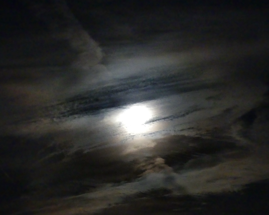 The full moon glowing behind some dramatic streaky clouds
