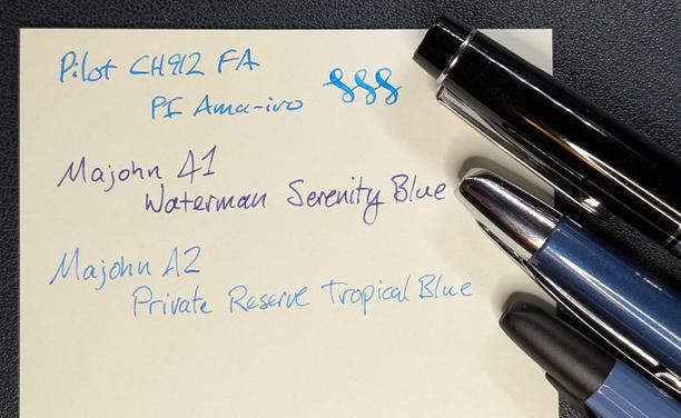 Photo of a writing sample and three fountain pens. The pen is next to its corresponding writing sample:

"Pilot CH912 FA / PI Ama-Iro" followed by three curlicues. The pen is black with silver trim. Only the cap is visible.

"Majohn A1 / Waterman Serenity Blue" The pen is a glossy medium blue with shiny silver trim. It is a round capless pen with the tip and clip visible.

"Majohn A2 / Private Reserve Tropical Blue" The pen is a matte blue with matte black trim. It is a faceted capless pen with the tip and clip visible.