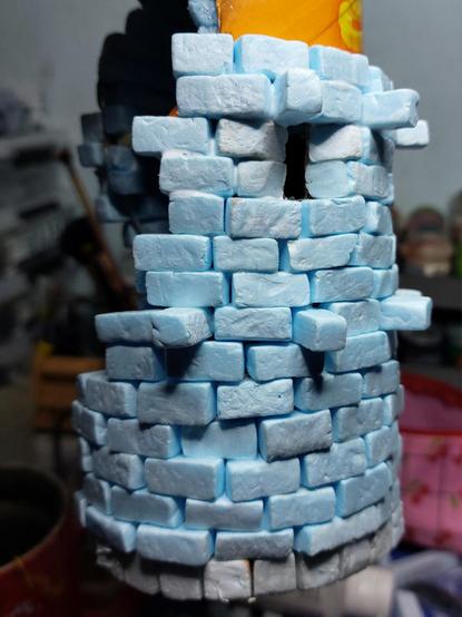 Pringles can with layers of rectangular stones on the outside. One Arrow slit is visible and it has tapered edges to allow for a wider field of vision and relaxed aiming and shooting at anyone contesting this piece of mordheim that the tower is stood on.