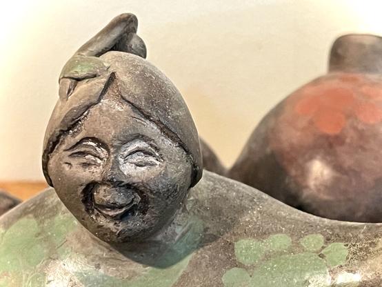 Lächelndes Gesicht einer Keramikfigur aus dunklem Ton.