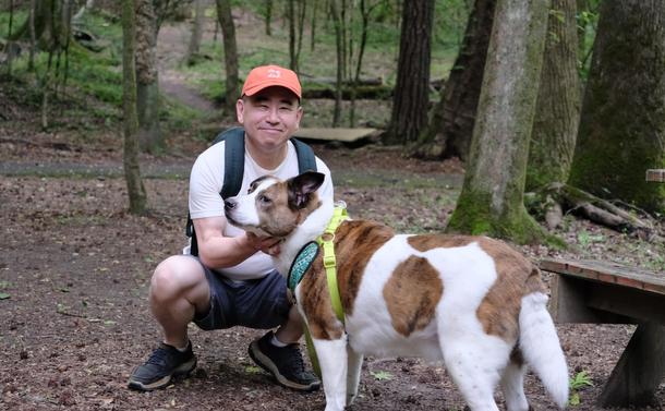 A man with an orange cap crouching in a park, holding his white and brown dog
