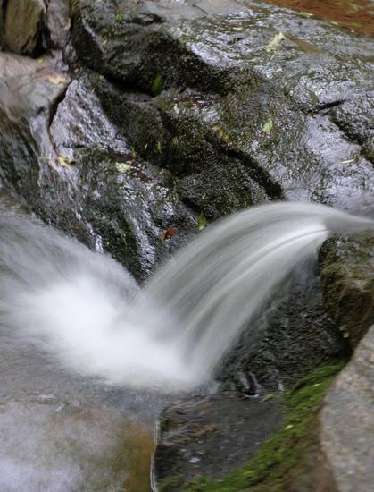 A tiny part of a waterfall in a park, water rushing down between large rocks