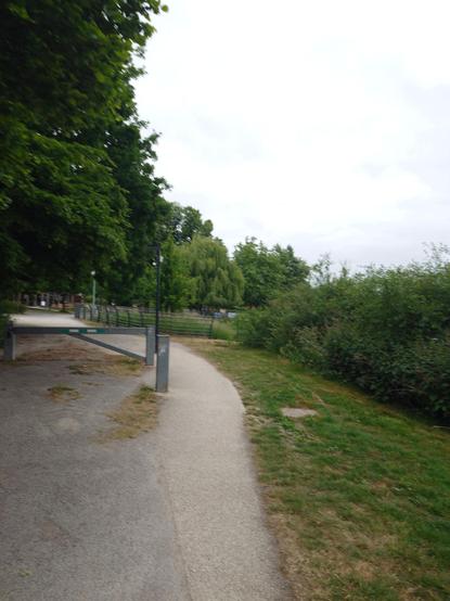 The pedestrian path with a vehicle lock. Vegetation all around. Cloudy sky.