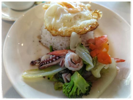 Dish with rice, a fried eggs, and vegetable. In between the vegetable are pieces of octopus and shrimps.