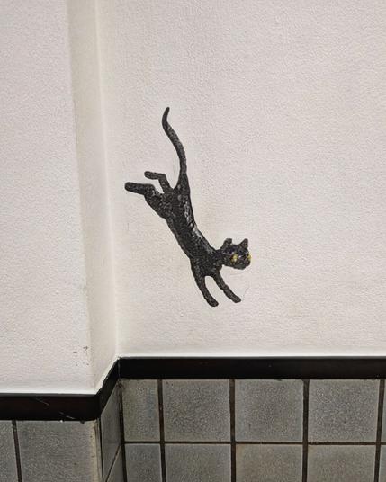 jumping black cat, drawn on a white wall with black/grey tiles on the bottom half

it appears as if the cat is jumping on the row of tiles