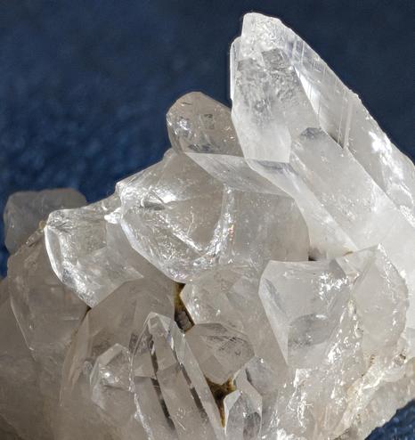 A macro photo of some details of a rock crystal cluster with several visible sharp crystal points, the one in the center has a tiny rainbow in it if you squint. The background is dark blue velveteen.  This is one of many I collected in the Hot Springs area of Arkansas in the early 1990s. Photo by Peachfront.