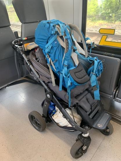 A HUGE blue backpack sitting in a baby buggy, with additional luggage stored below the seat. The buggy is located in a train. Don’t worry, I did not forget my baby, but he prefers to travel by carrier, so my back is already occupied…