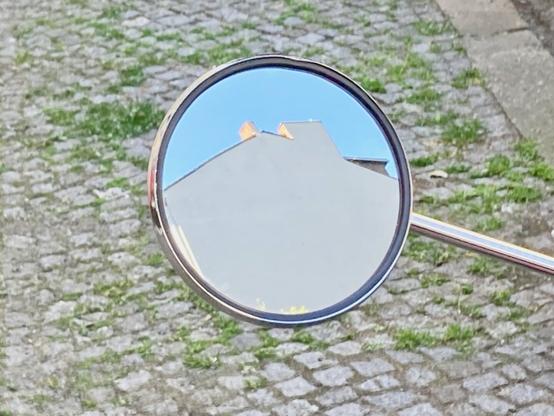 Blick in eine Spiegel eines Motorrollers. Es spiegelt sich eine Hausfassade und ein blauer Himmel.