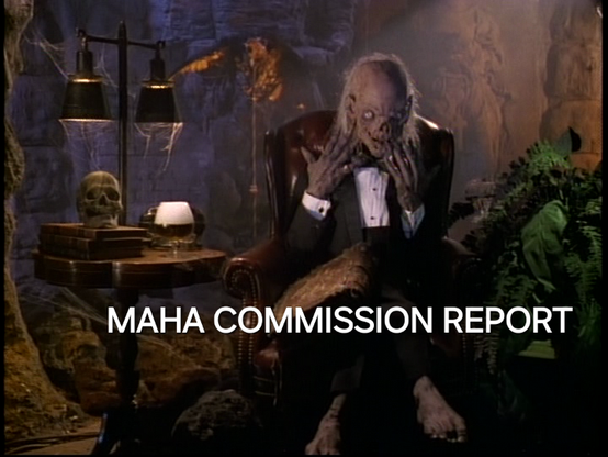 The zombie Crypt Keeper is in its cave, sitting in a brown leather chair. It is wearing a tuxedo and looking down at a large,  deteriorated book. A side table holds 3 old books with a skull sitting on top. The table lamp has black shades with spider webs hanging down. There is a large green plant with dying leaves next to the chair. The caption reads: MAHA COMMISSION REPORT