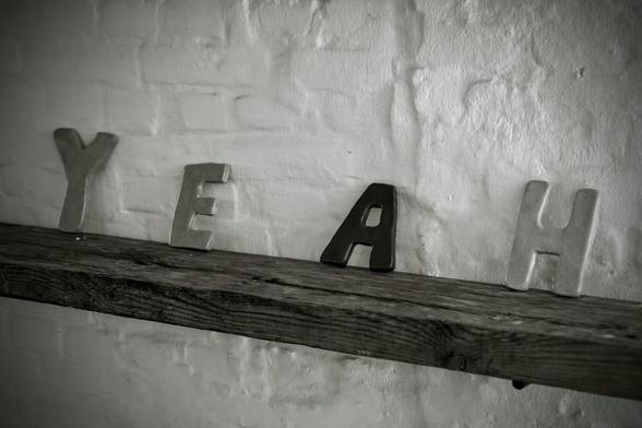 four letters spaced apart on a wooden board form the word: yeah