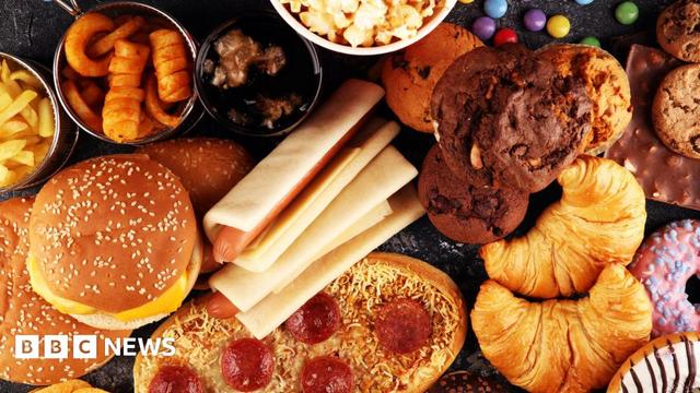 An overhead view of food which can be described as ultra-processed, including chocolate muffins, hot dogs, supermarket pizza, crisps, popcorn, doughnuts, burger buns and sweets