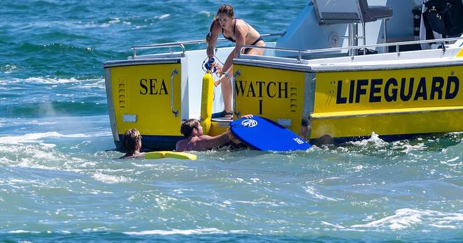 Newport Beach, CA - July 05: Newport Beach lifeguard Tyler Duss, left in water, assists fellow lifeguard Carly Christian. Newport Beach, CA - July 05: Newport Beach lifeguard Tyler Duss, left in water, assists fellow lifeguard Carly Christian.
