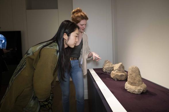 Two students carefully observing ancient stone objects in a gallery display