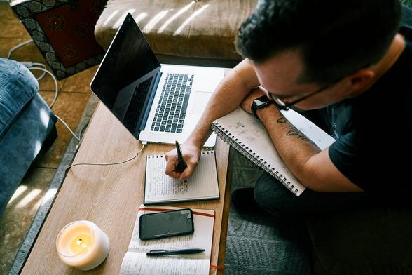 A man writes notes next to his laptop.