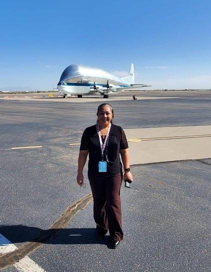 A person walks on a tarmac with a large, reflective aircraft in the background under a clear blue sky.