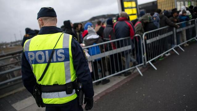 A Swedish police officer watches over a queue of newly arrived people, at Hyllie station outside Malmö, Sweden. 19 November 2015. | Copyright AP Photo