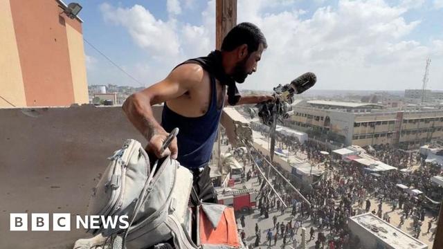 A man holds a microphone in one hand and a rucksack - both are covered in dust
