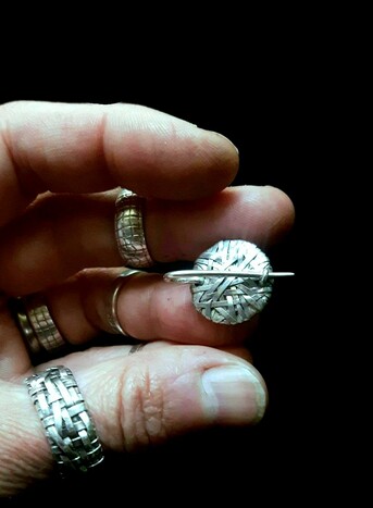 P Gurgel-Segrillo designer-maker holding a woven series small disc pin handcrafted in silver - back view