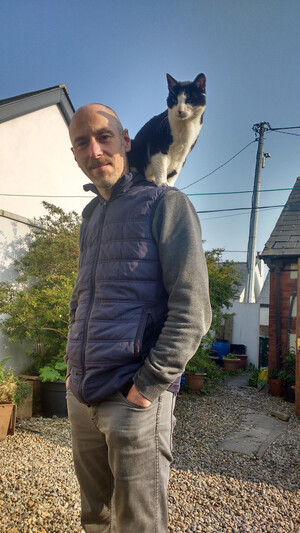 Photo of Molly cat perched on the shoulder of Bob's husband Leon in their garden.