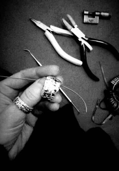 Designer maker P Gurgel-Segrillo at work: black amd white picture shows her hand holding a woven ring in the making, with jewellery making tools in the background.
