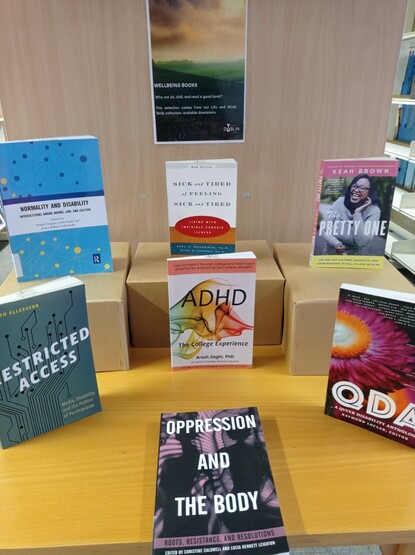 More books on disability. They are on a smaller table, with some stacked on boxes. Titles highlighted are Restricted Access, Queer Disability Anthology, The Pretty One, ADHD: The College Experience, Sick and Tired of being Sick and Tired, and Disability and Normality.