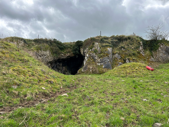 Mouth of a cave in Ireland surrounded by green grass on a hill 