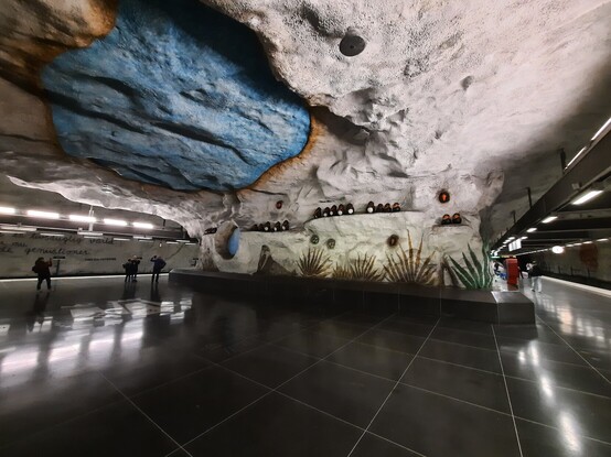 Art: Penguins sit along a wall over a mural of a seal and a painting of a watering hole. Another watering hole is painted on the roof in an underground train station in Stockholm, Sweden. 